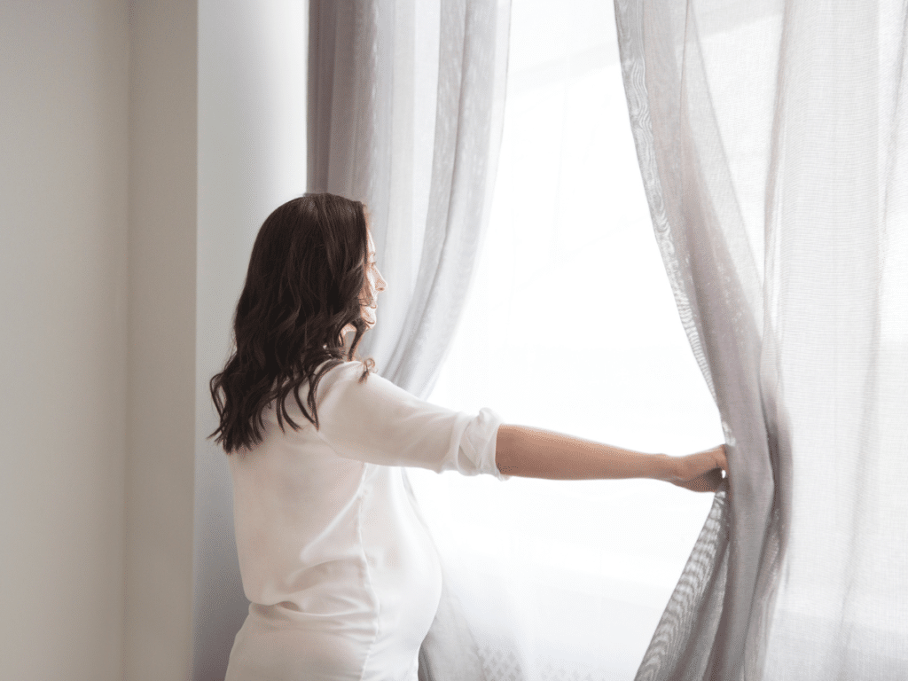 woman looking out the window with curtains